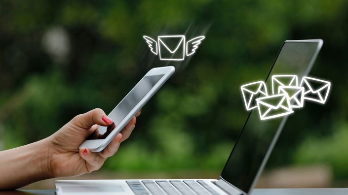 Uma pessoa enviando um email com informações com um celular e no laptop
