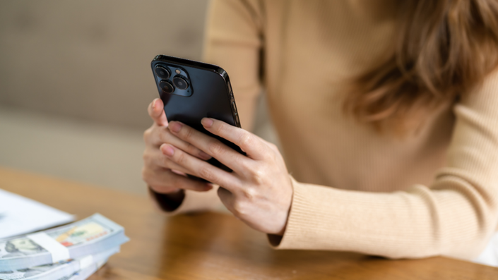 Mulher sentada com dinheiro sobre a mesa e mexendo no celular