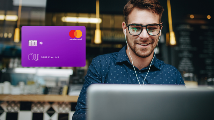 Hombre con gafas y camisa azul de botones, sonriendo mientras usa su laptop en un café con una decoración moderna e iluminación cálida