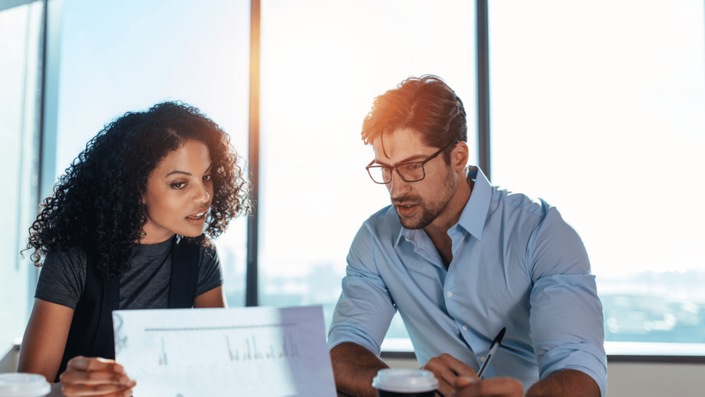 Dos personas analizando gráficos financieros en una oficina con luz natural, discutiendo estrategias para invertir en fondos de inversión en México.