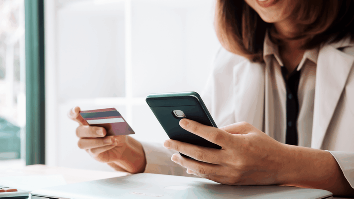 Mulher consultando no celular informações sobre a portabilidade da dívida do cartão de crédito que segura.